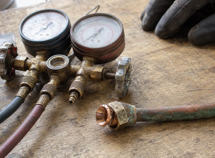 A worn HVAC gauge manifold and a freshly cut copper flare fitting resting on a scarred wooden workbench.